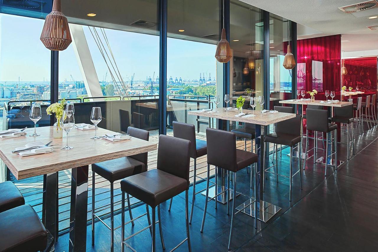The Westin Hamburg Elbphilharmonie Hotel Екстериор снимка The photo depicts a modern restaurant interior featuring a spacious dining area with large windows that provide a view of the outside. There are several tall tables with a light-colored surface and metallic bases, accompanied by dark, sleek stools. T
