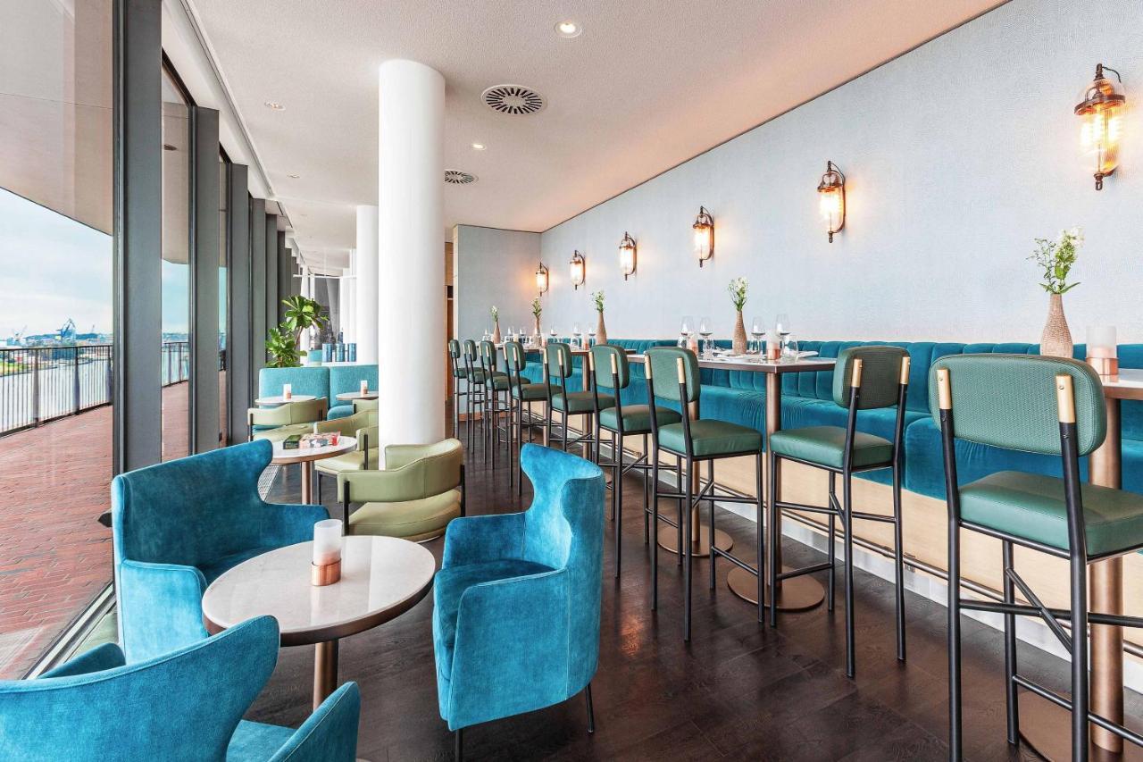 The Westin Hamburg Elbphilharmonie Hotel Екстериор снимка The photo shows a modern and stylish restaurant or café interior. It features a long row of high-backed bar stools at a counter, complemented by plush seating in the form of rounded chairs and small tables arranged throughout the space. The color sch