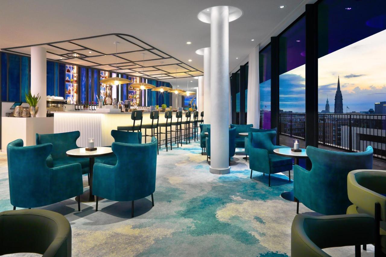 The Westin Hamburg Elbphilharmonie Hotel Екстериор снимка The photo shows a modern lounge or bar area with a stylish design. It features plush turquoise chairs and small tables arranged around the space. In the background, there's a long bar with seating, illuminated by soft lighting. Large windows provide 