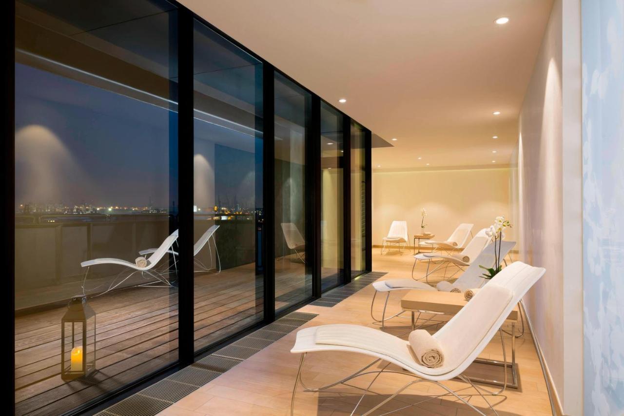 The Westin Hamburg Elbphilharmonie Hotel Екстериор снимка The photo shows a modern, stylish indoor space with large glass windows that offer a view of the night. The area is illuminated softly, highlighting a sleek and minimalist design. There are several white lounge chairs arranged on a wooden deck, creat