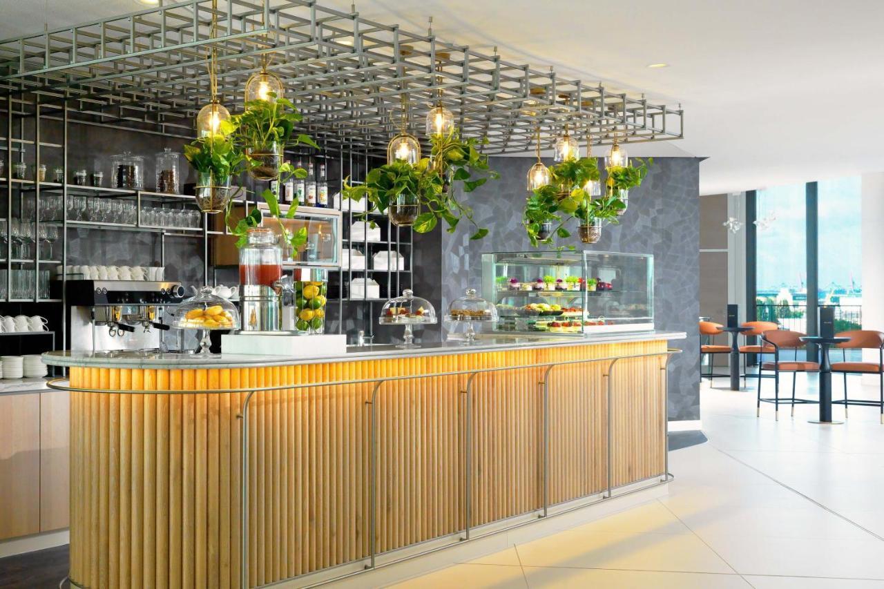 The Westin Hamburg Elbphilharmonie Hotel Екстериор снимка The photo shows a modern café or bar setting with a sleek wooden counter that features vertical slats. Above the counter, there is a grid-like framework hanging from the ceiling, adorned with various green plants that add a touch of nature to the int