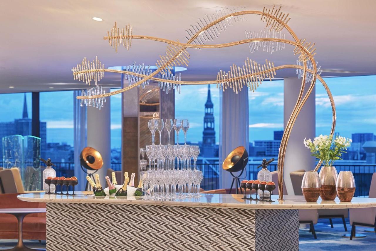 The Westin Hamburg Elbphilharmonie Hotel Екстериор снимка The photo depicts a stylish bar setup in a modern venue. The bar features an elegant design with a patterned front and a sleek countertop. Above the bar, there is a striking decorative element that resembles a stylized tree or wave, made from metalli