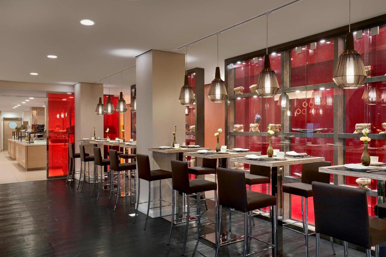 The Westin Hamburg Elbphilharmonie Hotel Екстериор снимка The photo shows a modern restaurant interior featuring a sleek, contemporary design. There are high tables with bar stools arranged along one side, illuminated by stylish hanging pendant lights. The color scheme includes warm tones, with red accents 