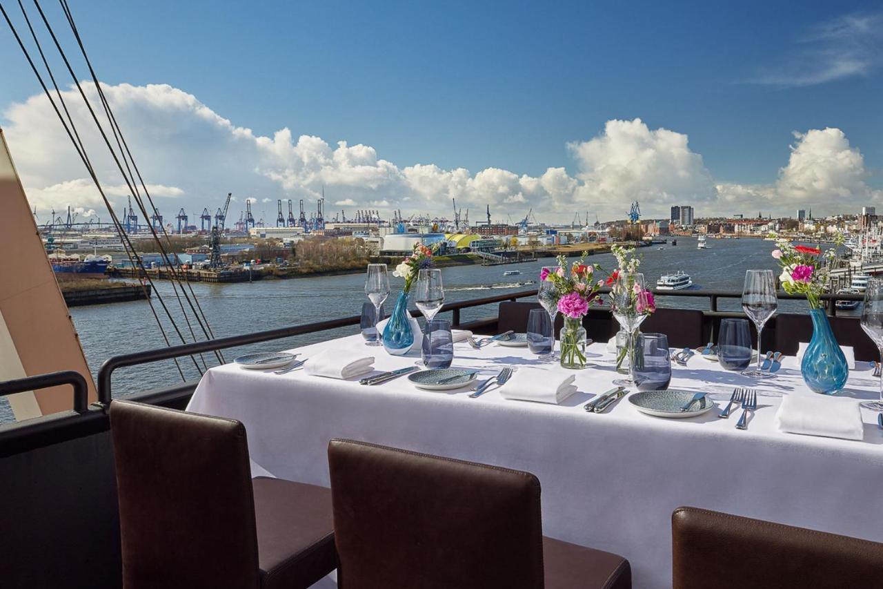 The Westin Hamburg Elbphilharmonie Hotel Екстериор снимка The photo shows a beautifully set dining table on a rooftop or terrace with a view of a body of water. The table is adorned with a white tablecloth, elegant tableware, and multiple vases filled with colorful flowers. In the background, there are boat
