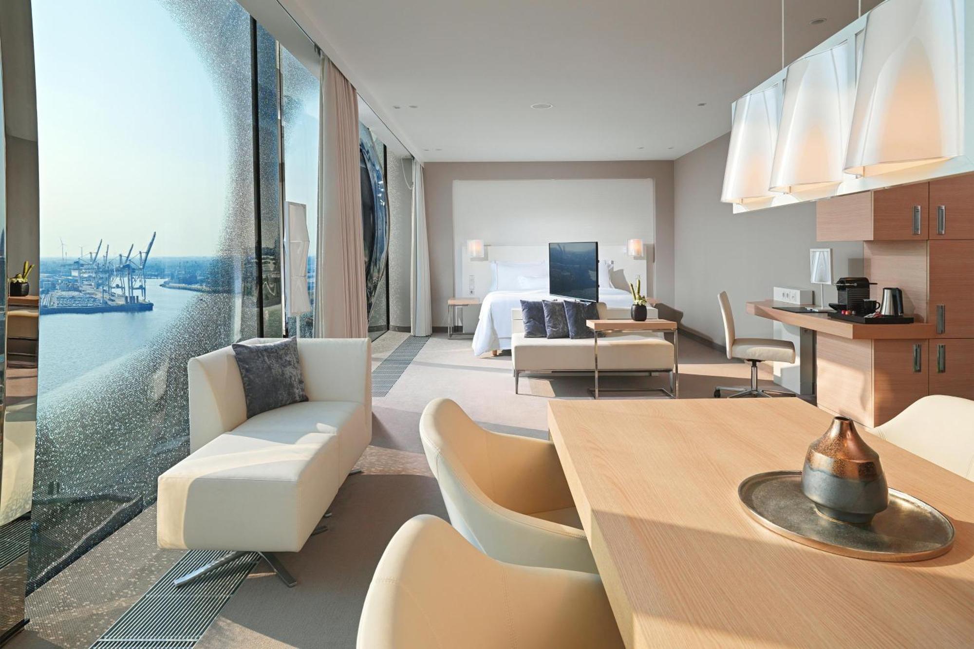 The Westin Hamburg Elbphilharmonie Hotel Екстериор снимка The photo shows a modern hotel room with a spacious layout. On one side, there are large floor-to-ceiling windows that offer a view of the outside, likely showcasing a waterfront or cityscape. Inside, there's a bed with a minimalist design, accompani