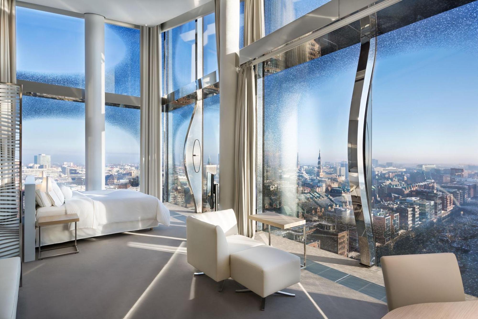 The Westin Hamburg Elbphilharmonie Hotel Екстериор снимка The photo shows a modern hotel room with a stunning, panoramic view through large, uniquely designed windows. The room features a sleek, minimalist aesthetic with light-colored furnishings, including a white bed and a couple of chairs. The walls are 